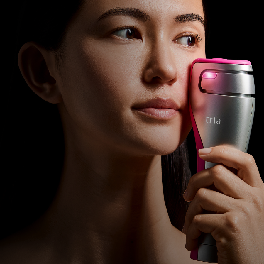 Woman using a Tria FRX laser device on her face with a dark background
