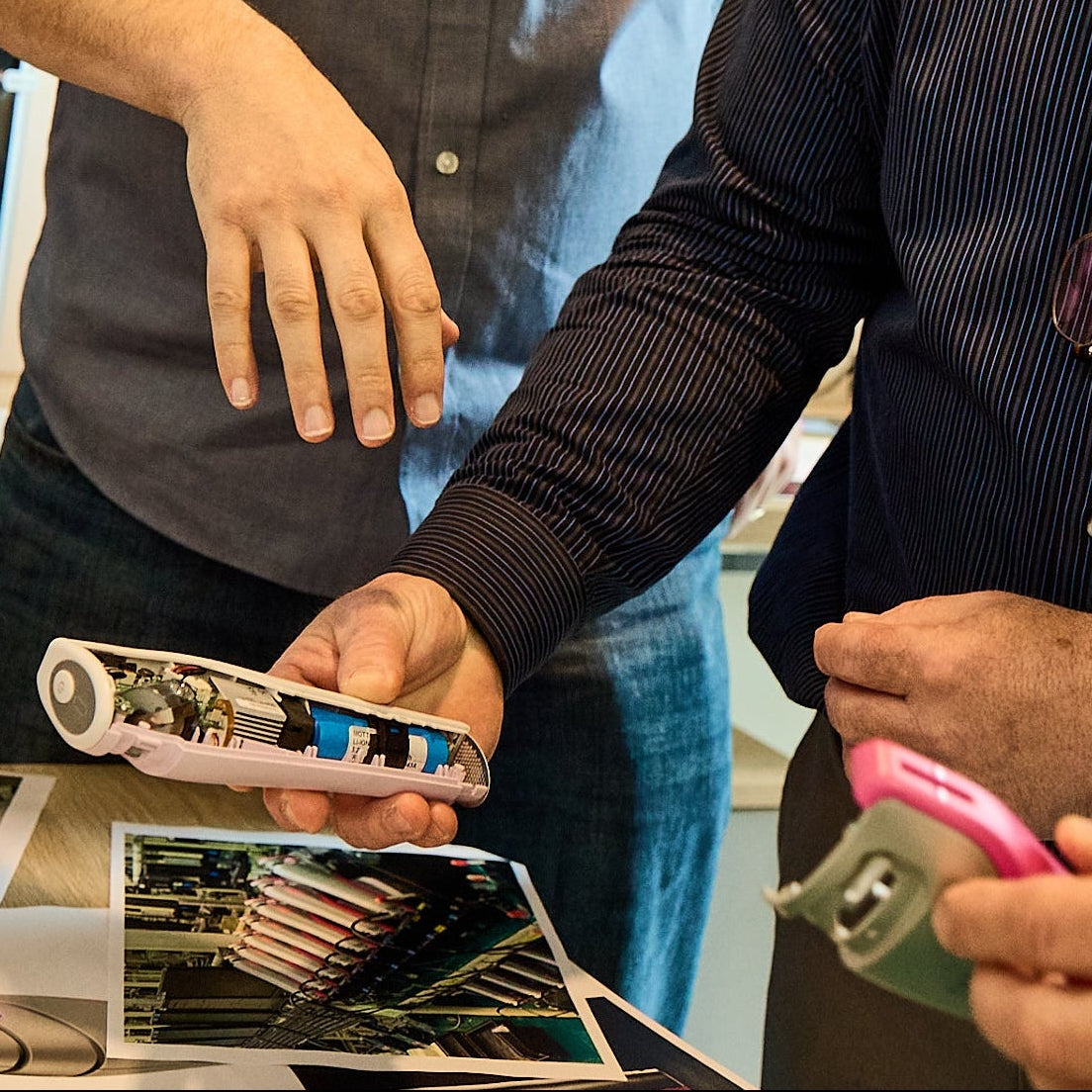 Three men in a workshop, looking at a Tria FRX Skin Rejuvenation device together.